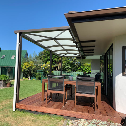 Outdoor patio area with wooden deck, table, and chairs under a pergola on a sunny day.